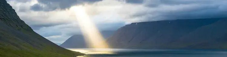 una luz traspasando unas nubes en medio de montanas